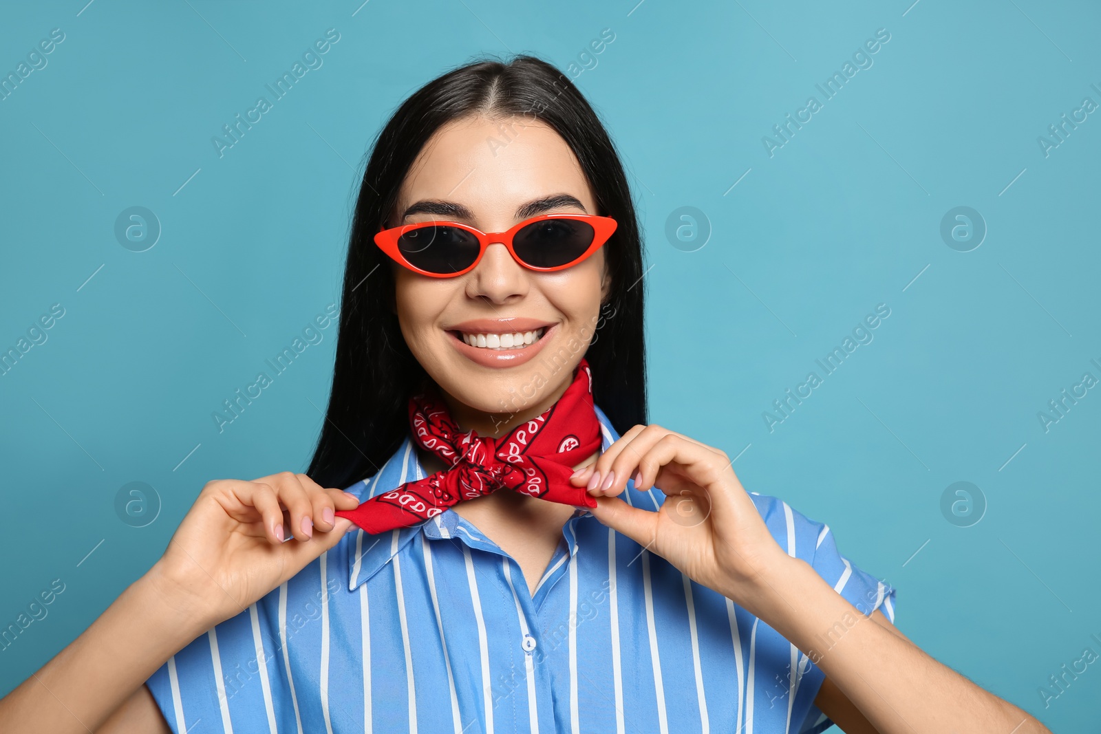 Photo of Fashionable young woman in stylish outfit with bandana on light blue background