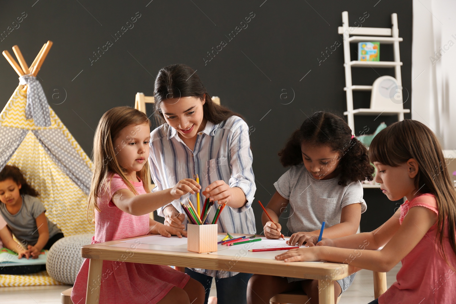 Photo of Cute little children with nursery teacher drawing at table in kindergarten. Indoor activity