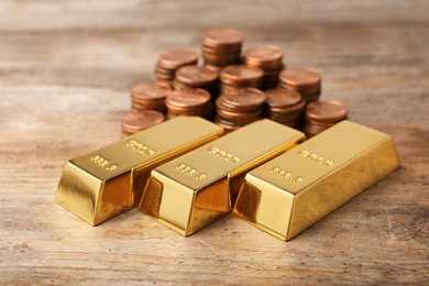 Shiny gold bars and coins on wooden background