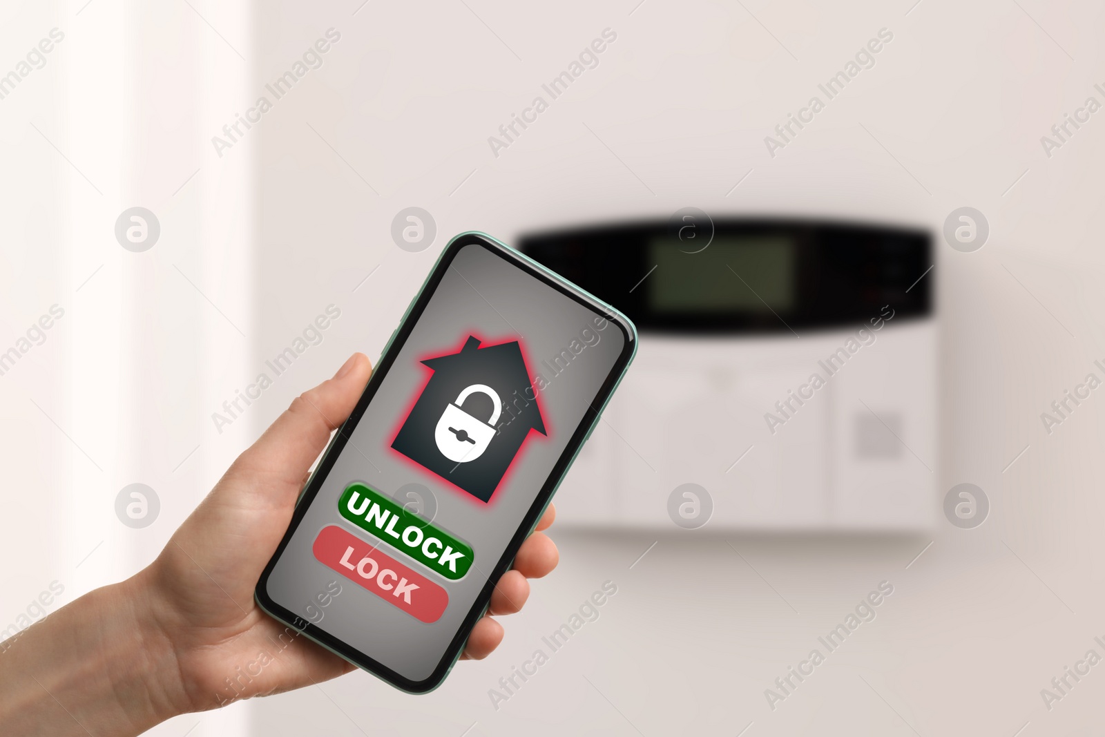 Image of Woman operating home alarm system via mobile phone against white wall with security control panel, closeup. Application interface on device screen