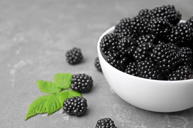 Bowl with ripe blackberries and leaves on grey table, closeup