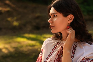 Photo of Beautiful woman in embroidered shirt outdoors on sunny day, space for text. Ukrainian national clothes