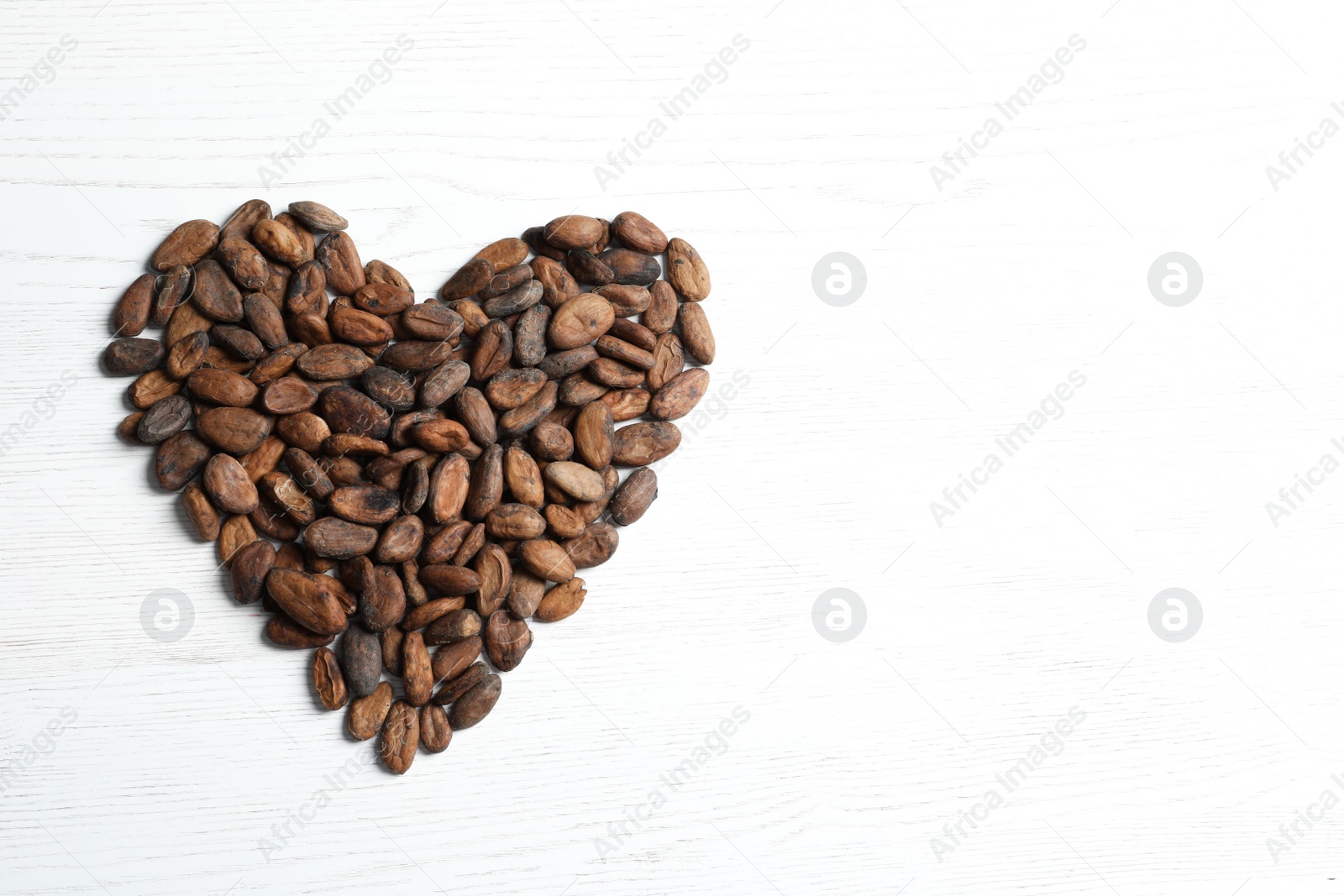 Photo of Heart made of cocoa beans on white wooden table, top view. Space for text
