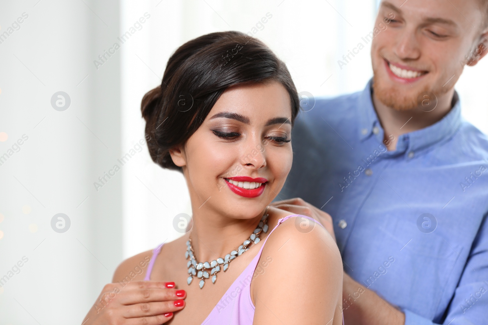 Photo of Man putting elegant jewelry on beautiful woman against light background