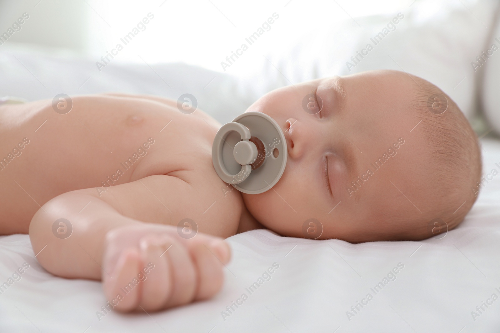 Photo of Cute little baby with pacifier sleeping on bed, closeup