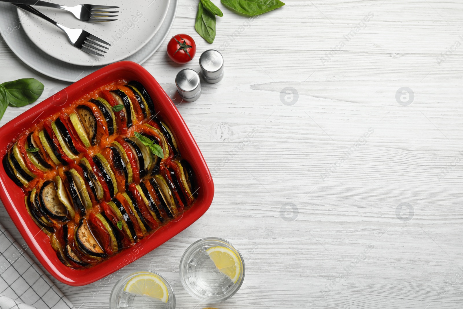 Photo of Delicious ratatouille in baking dish on white wooden table, flat lay. Space for text