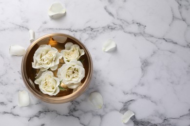 Photo of Tibetan singing bowl with water and beautiful roses on white marble table, top view. Space for text