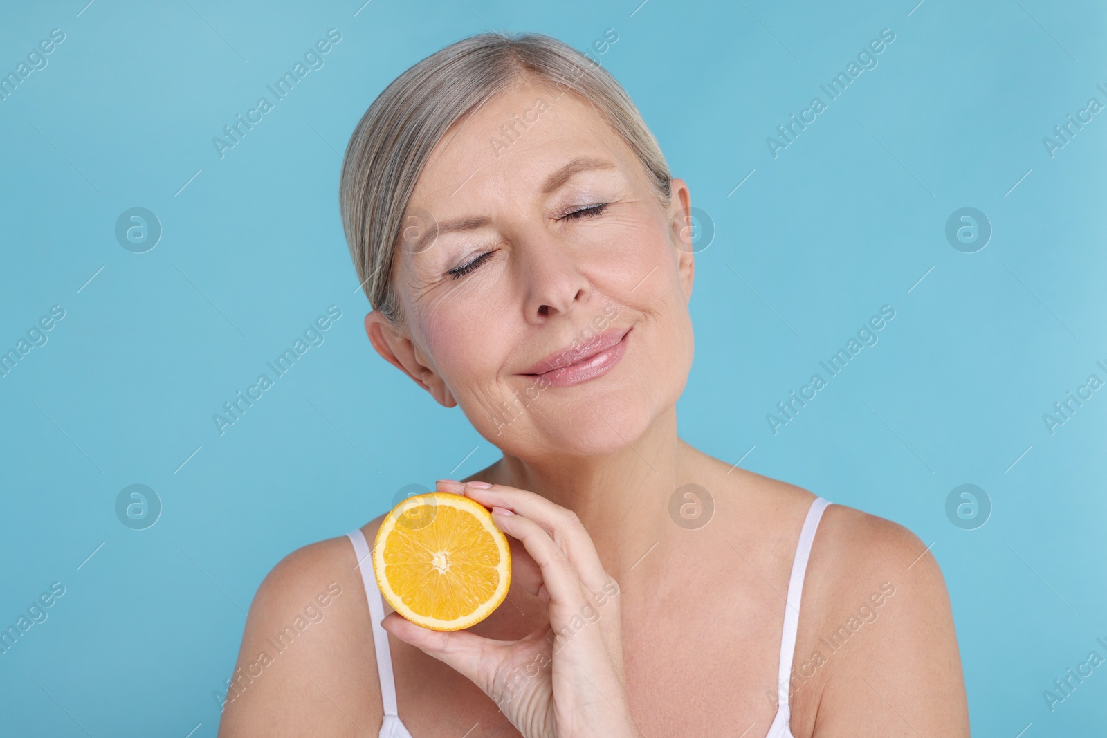 Photo of Beautiful woman with half of orange rich in vitamin C on light blue background