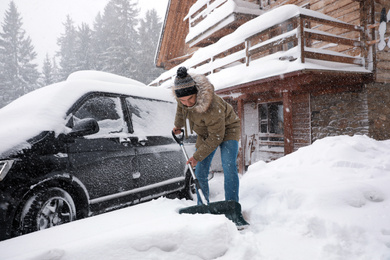 Photo of Young man cleaning snow with shovel near his house