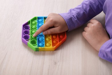 Photo of Little child playing with pop it fidget toy at wooden table, closeup