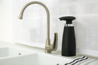 Photo of Modern automatic soap dispenser near sink in kitchen