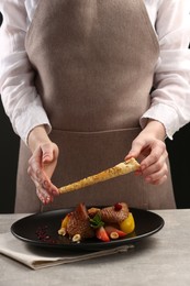 Photo of Food stylist preparing delicious dish with chicken, parsnip and strawberries for photoshoot at grey table in studio, closeup