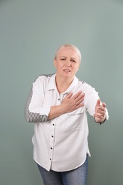 Mature woman having heart attack on color background