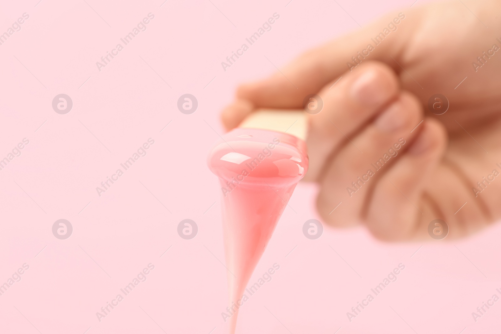 Photo of Woman holding spatula with hot depilatory wax on light background, closeup. Space for text