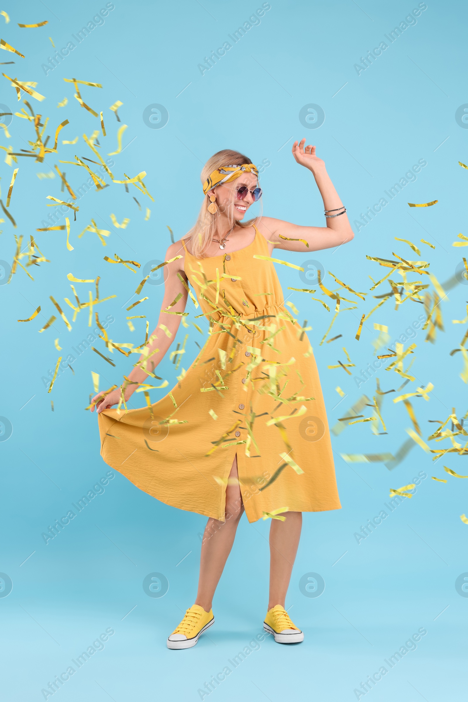 Image of Happy woman dancing under falling confetti on light blue background