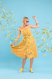 Image of Happy woman dancing under falling confetti on light blue background