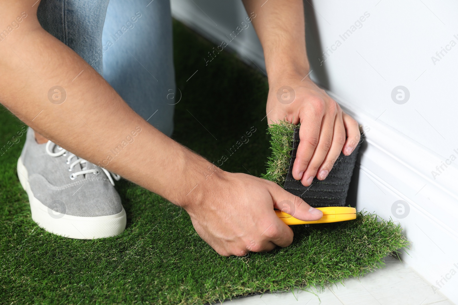 Photo of Man cutting artificial grass carpet indoors, closeup