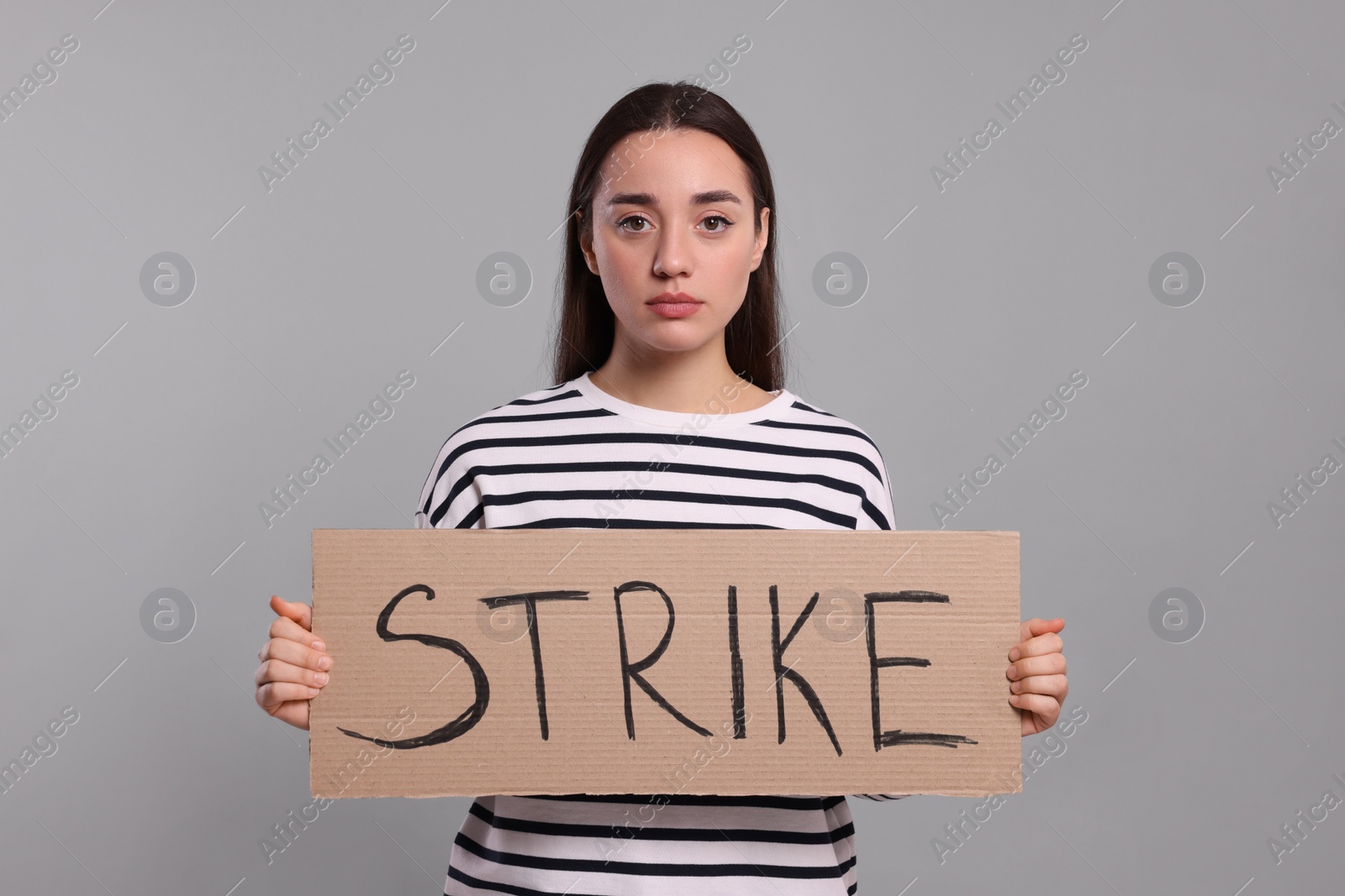 Photo of Young woman holding cardboard banner with word Strike on light grey background