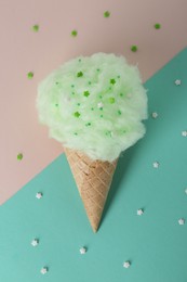 Sweet cotton candy in waffle cone on color background, top view