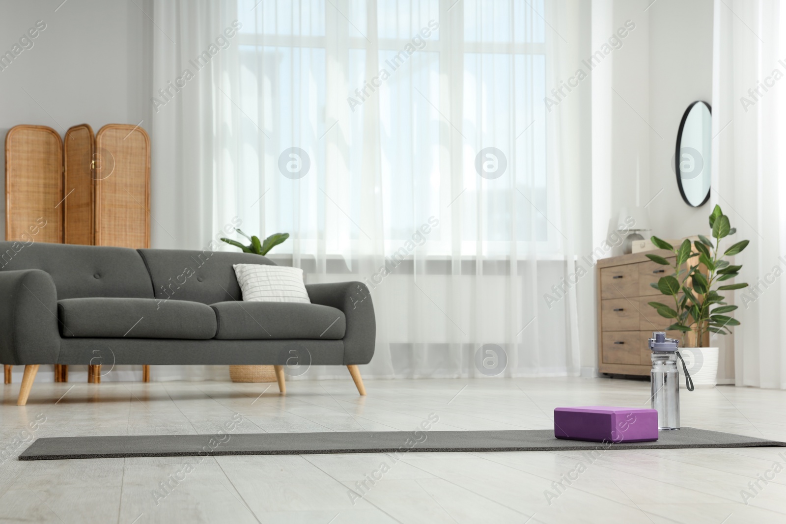 Photo of Exercise mat, yoga block and bottle of water on floor in room