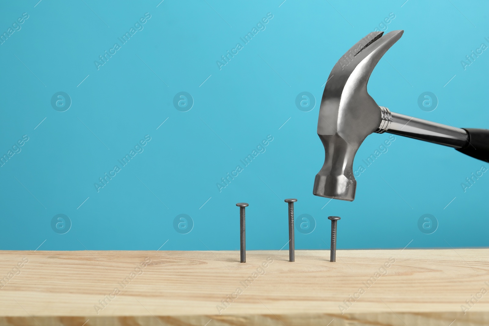 Photo of Hammering nail into wooden surface against light blue background, space for text