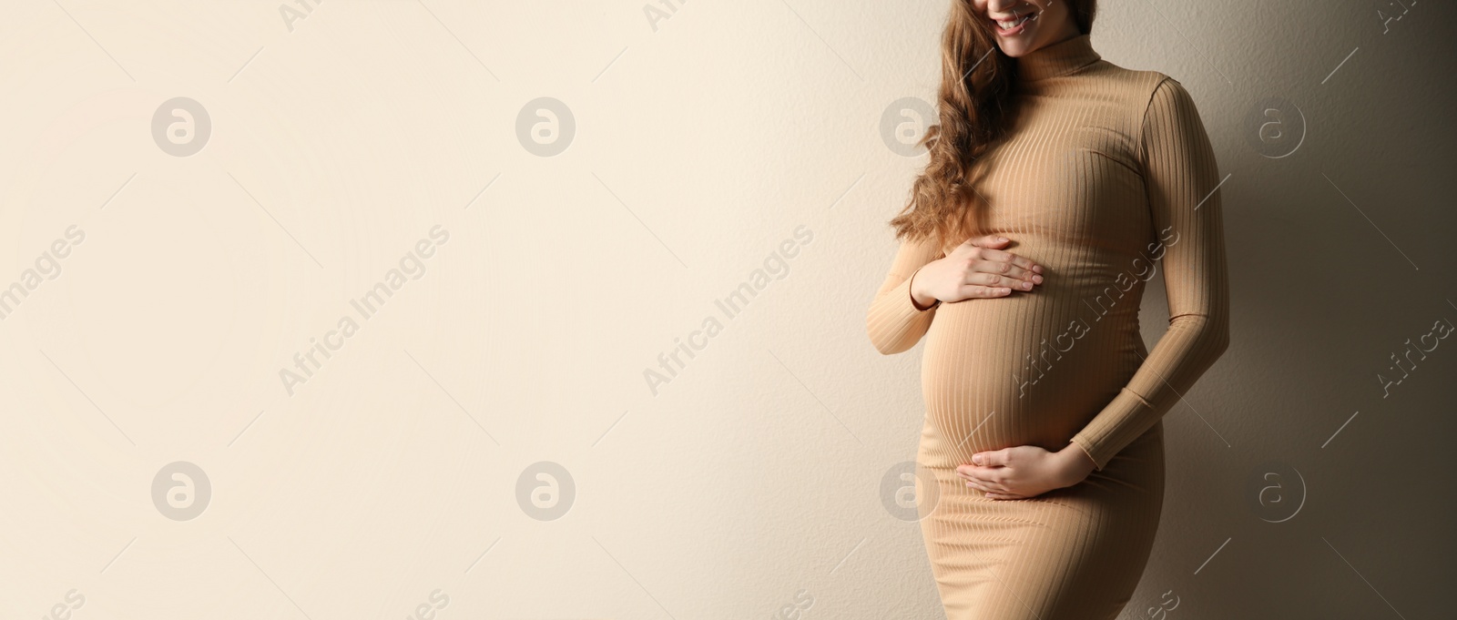 Image of Pregnant woman touching her belly on beige background, space for text. Banner design