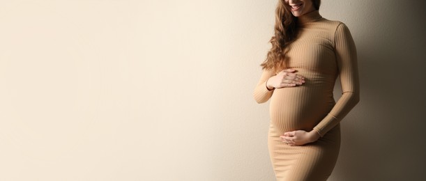 Pregnant woman touching her belly on beige background, space for text. Banner design