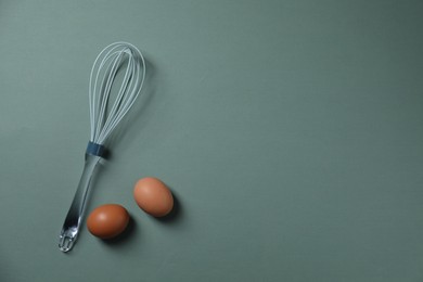 Photo of Whisk and raw eggs on pale blue background, flat lay. Space for text
