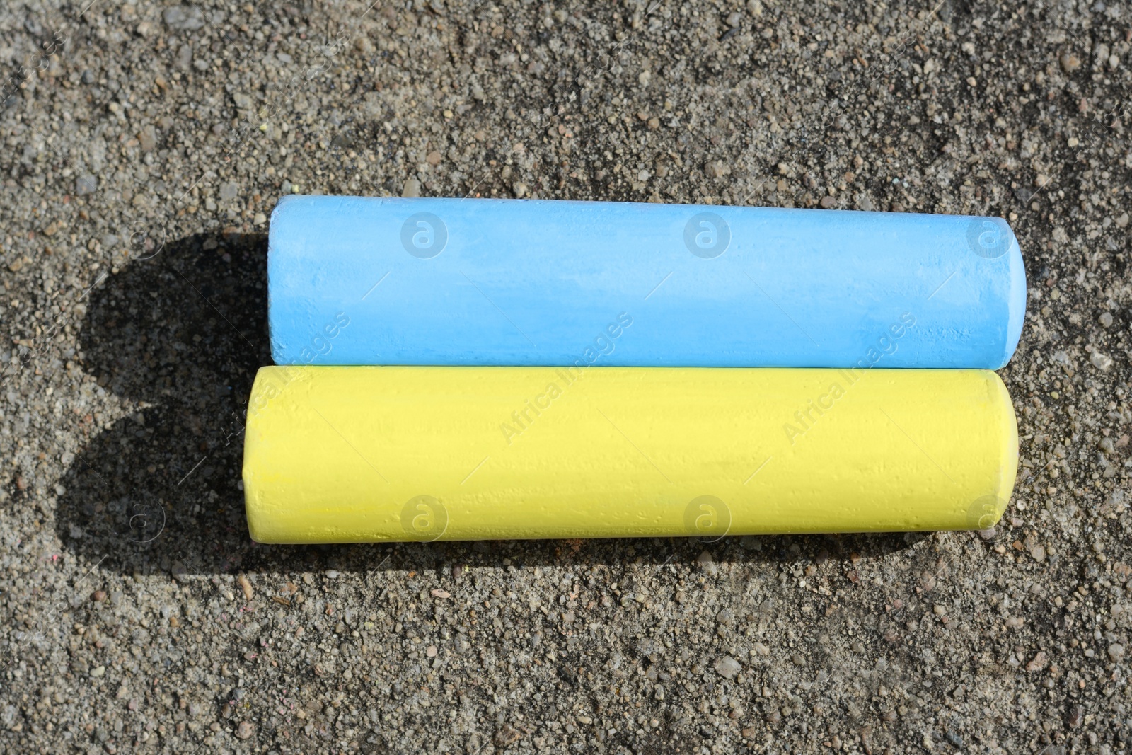 Photo of Yellow and light blue chalk sticks on asphalt, flat lay