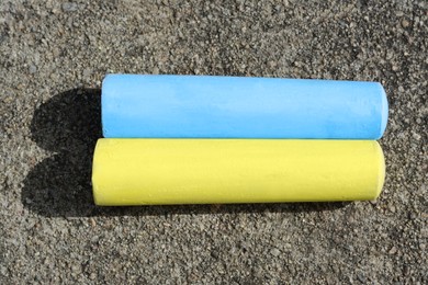 Photo of Yellow and light blue chalk sticks on asphalt, flat lay