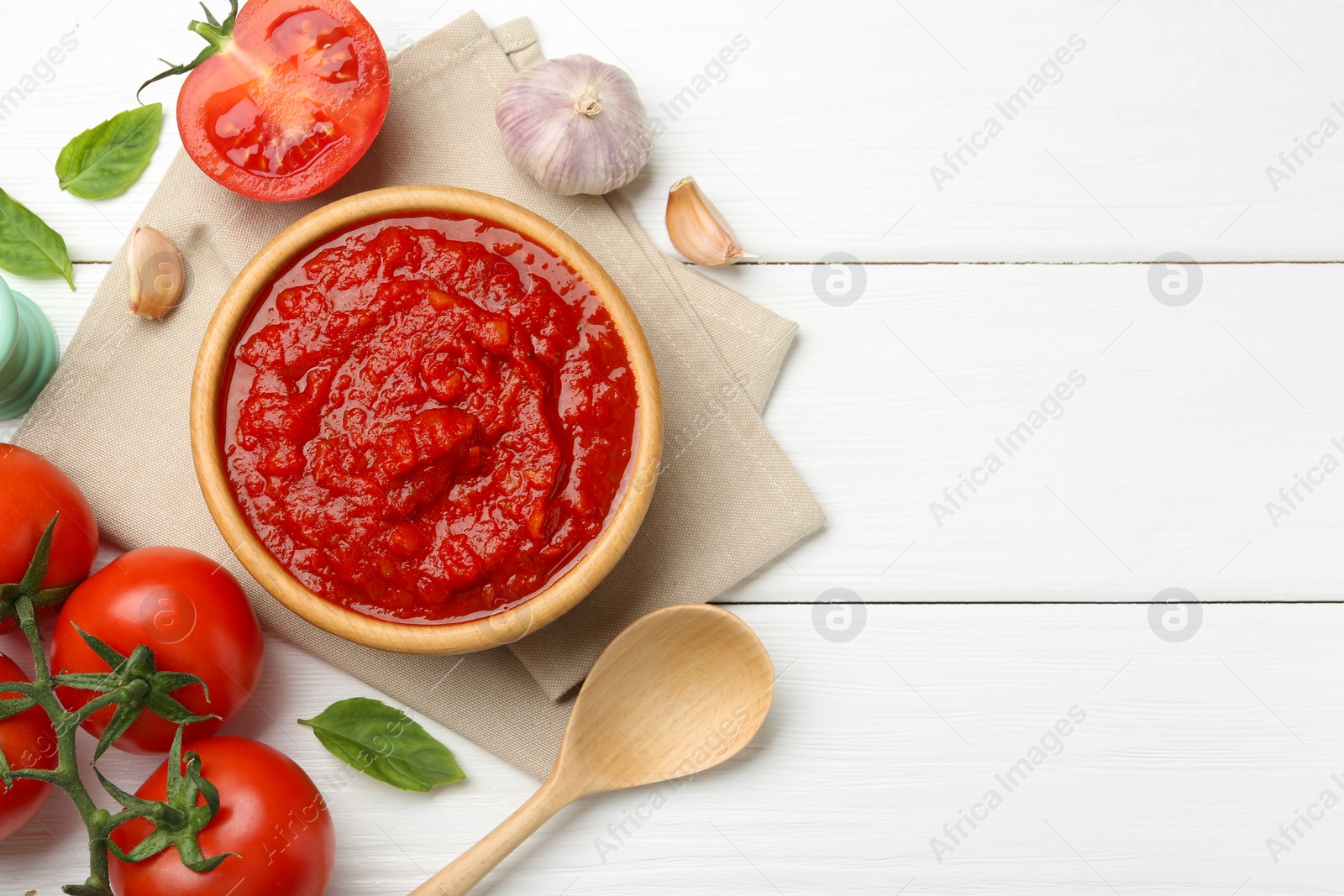 Photo of Homemade tomato sauce in bowl, spoon and fresh ingredients on white wooden table, flat lay. Space for text