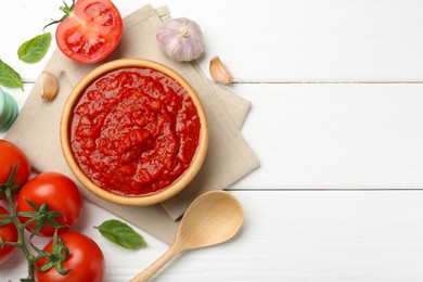 Photo of Homemade tomato sauce in bowl, spoon and fresh ingredients on white wooden table, flat lay. Space for text