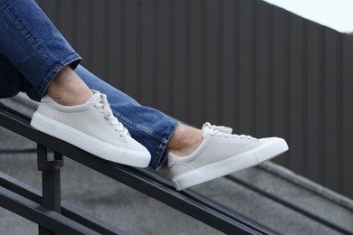 Photo of Man in stylish sneakers sitting on railing outdoors, closeup