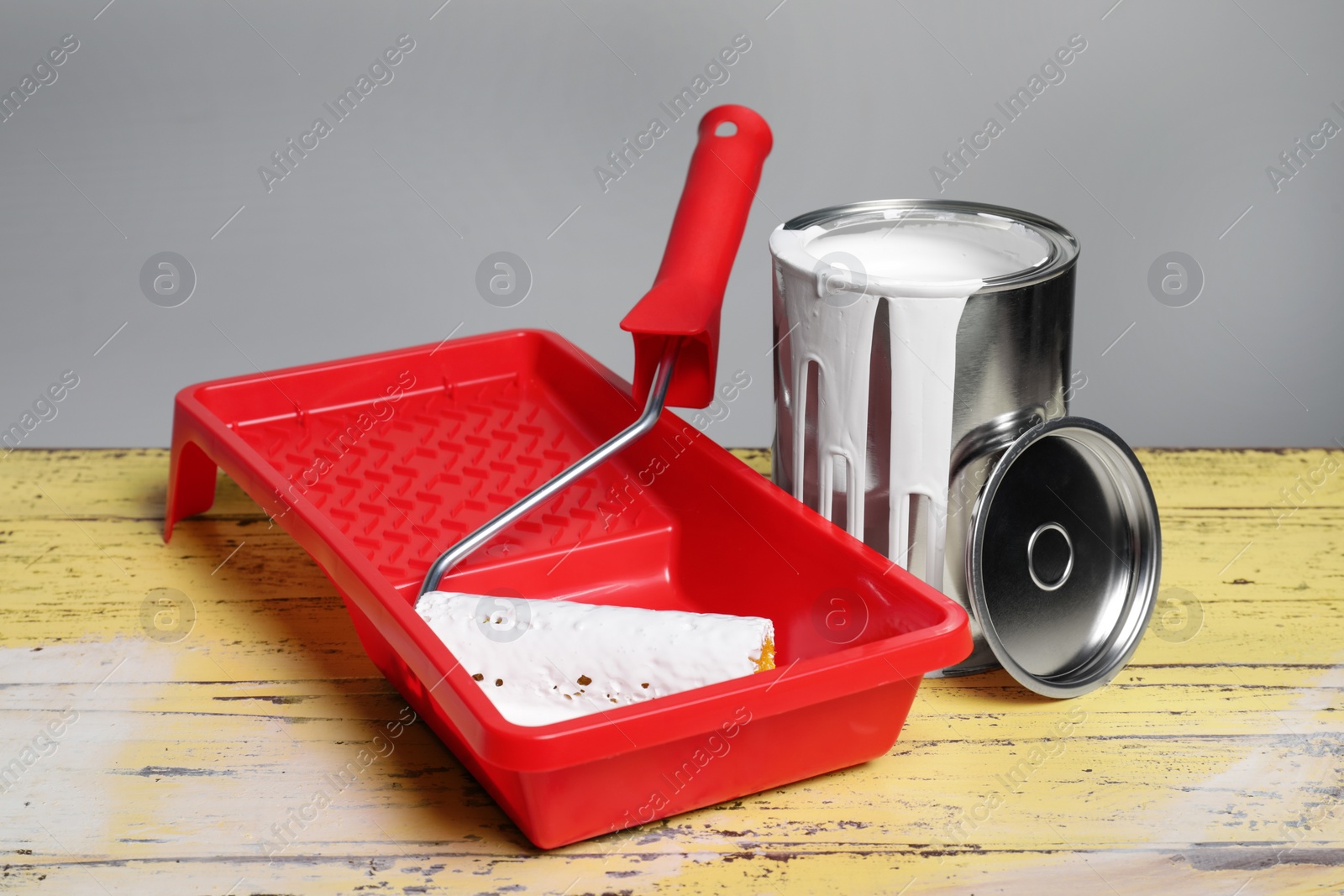 Photo of Can of paint and tray with roller on yellow wooden table