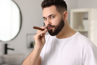 Photo of Handsome young man shaving beard with blade indoors