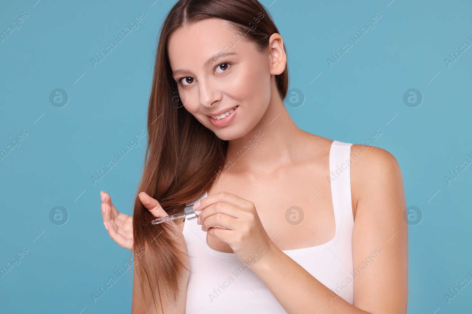 Photo of Beautiful woman applying serum onto hair on light blue background