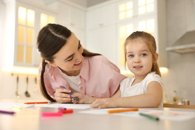 Photo of Mother and her little daughter drawing with colorful markers at table in kitchen