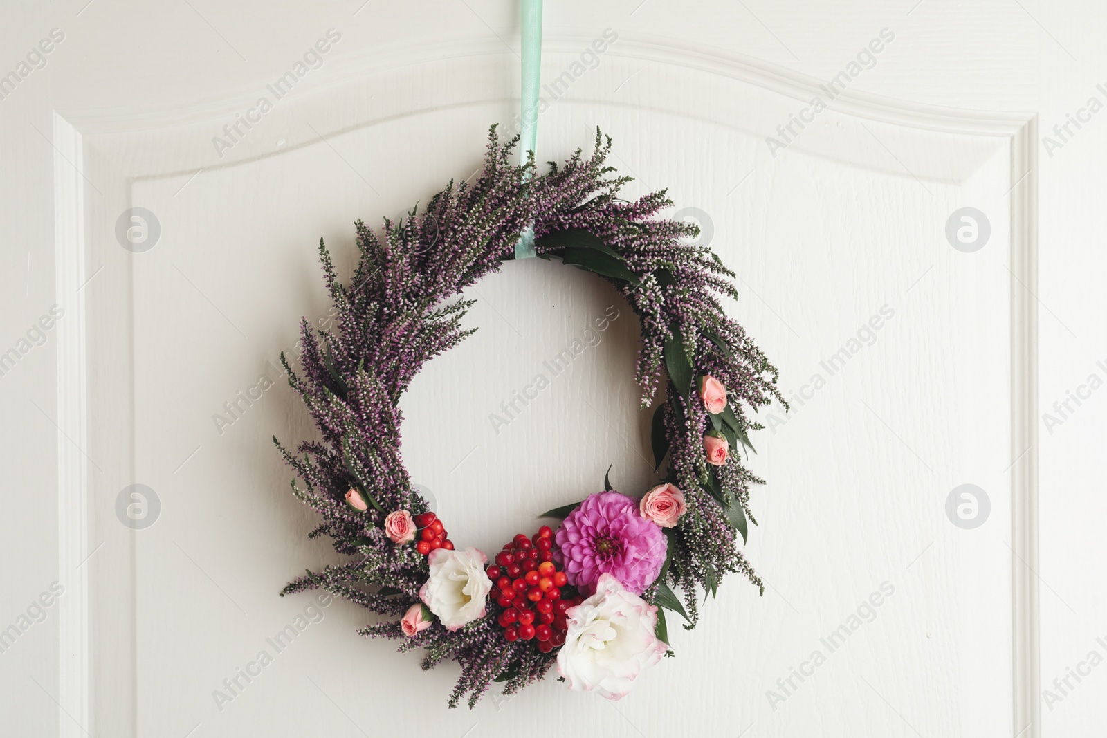 Photo of Beautiful autumnal wreath with heather flowers hanging on white wooden door. Space for text