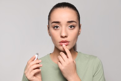 Woman with herpes applying cream on lips against light grey background