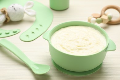 Plastic dishware with healthy baby food on white wooden table, closeup. Space for text