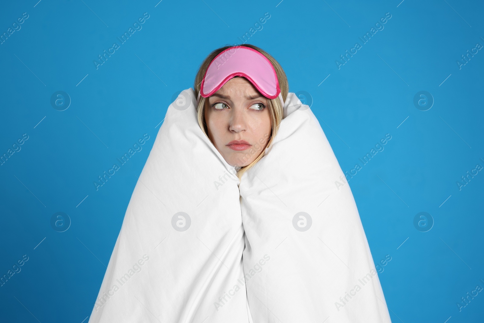 Photo of Young woman in sleeping mask wrapped with soft blanket on blue background