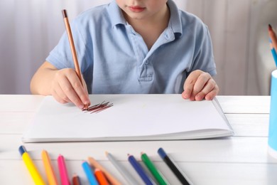 Photo of Little boy drawing with pencil at white wooden table indoors, closeup. Child`s art