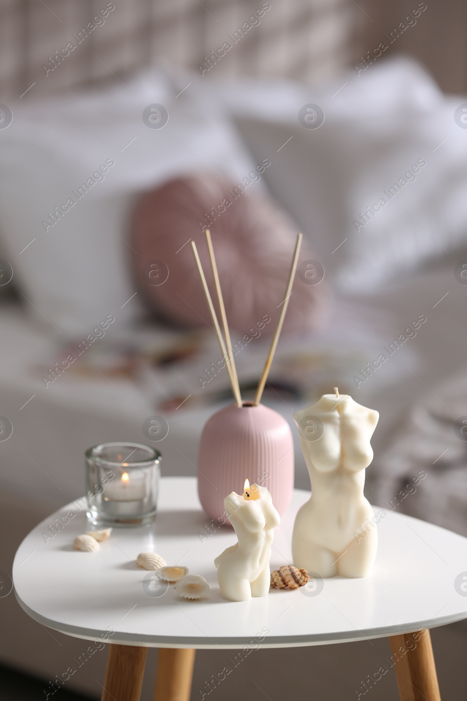 Photo of Beautiful body shaped candles, seashells and air reed freshener on table indoors