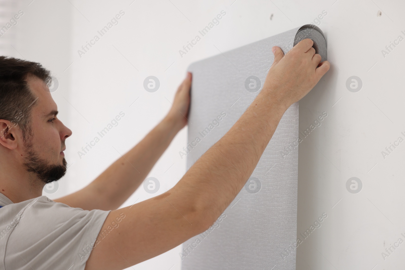 Photo of Man hanging stylish gray wallpaper in room