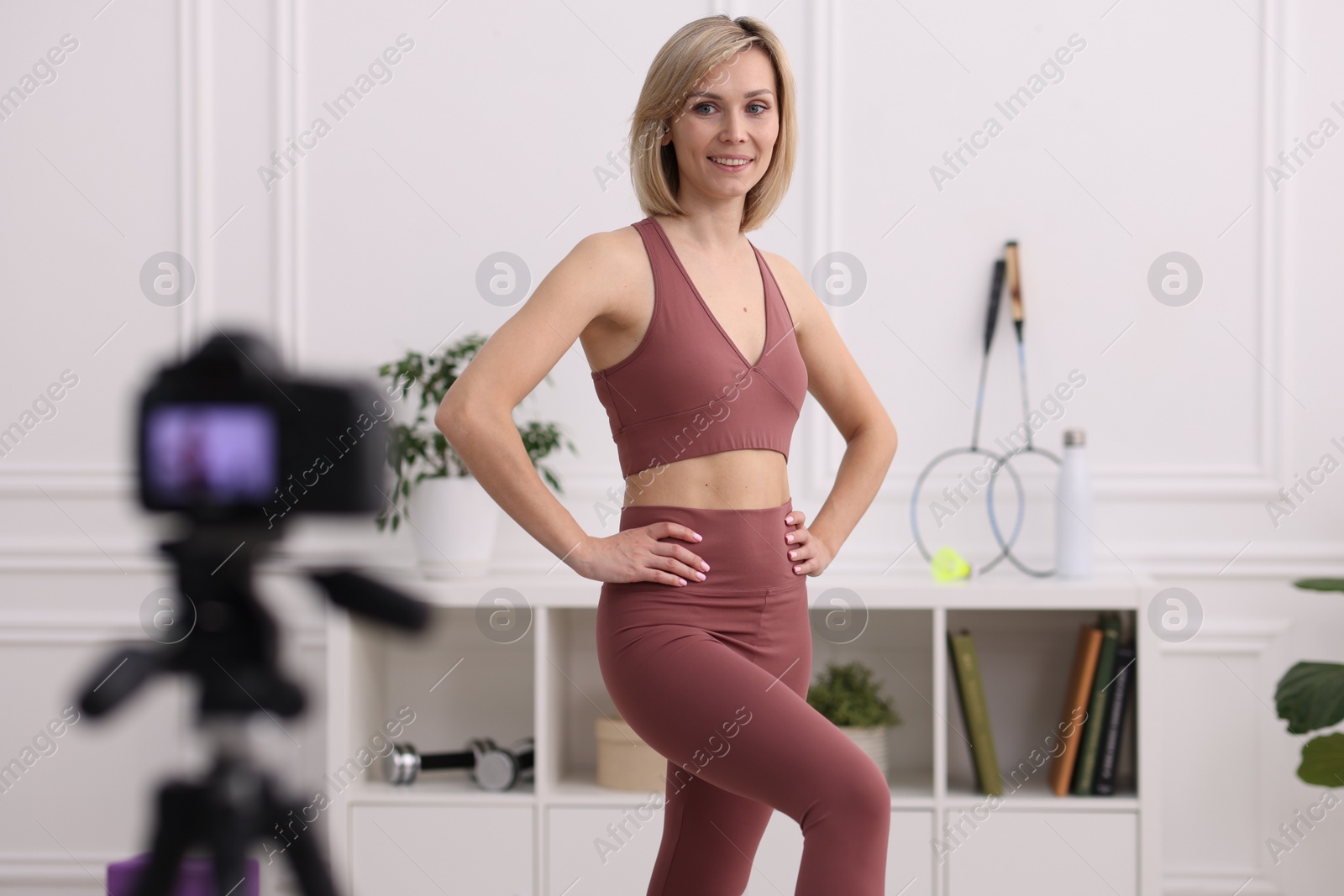 Photo of Smiling sports blogger recording fitness lesson with camera at home