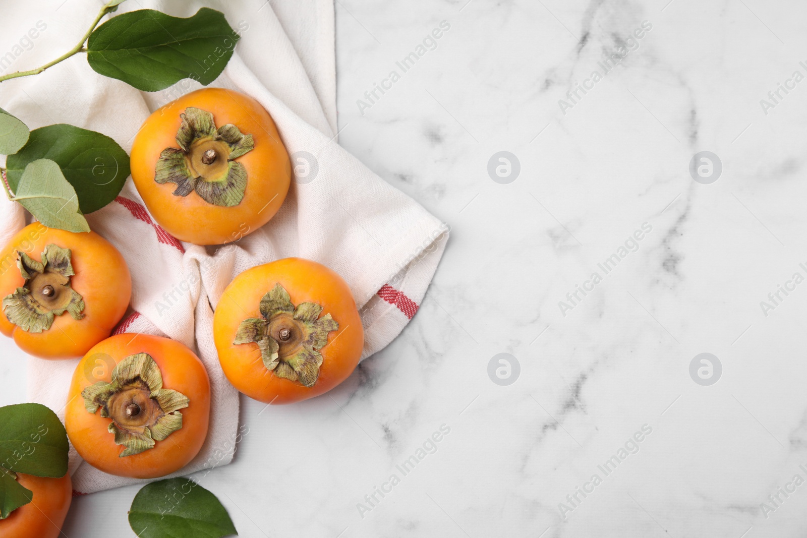 Photo of Delicious ripe juicy persimmons on white marble table, flat lay. Space for text