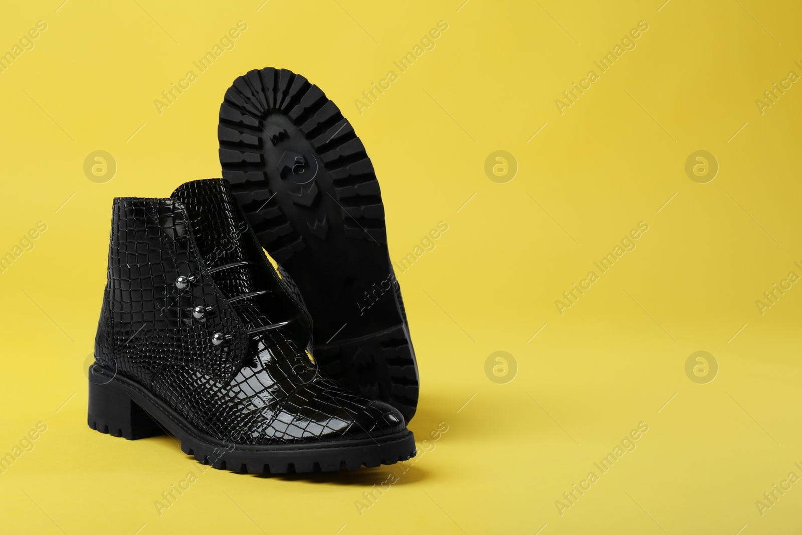 Photo of Pair of stylish ankle boots on yellow background. Space for text