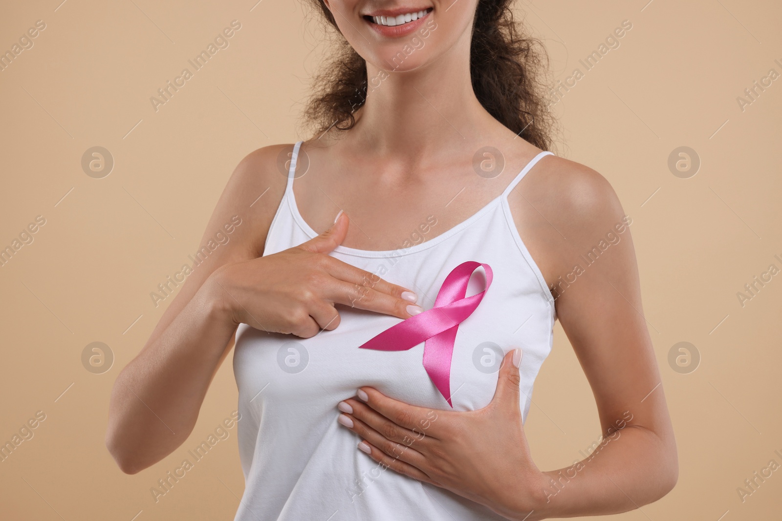 Photo of Breast cancer awareness. Woman with pink ribbon doing self-examination on light brown background, closeup