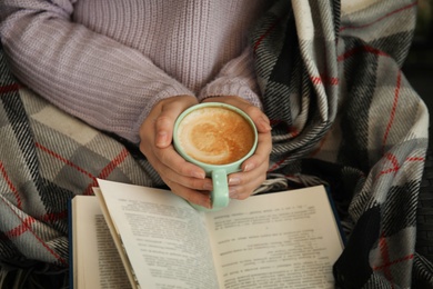 Photo of Woman with cup of coffee reading book at home, closeup