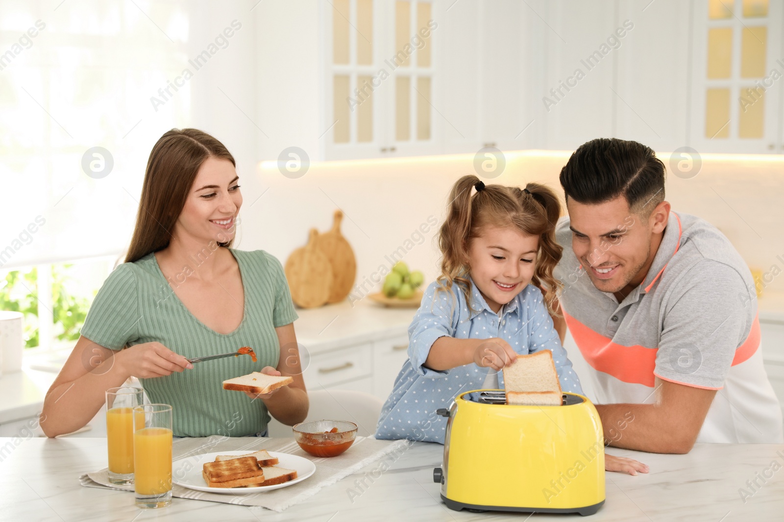 Photo of Happy family having breakfast with toasted bread at table in kitchen